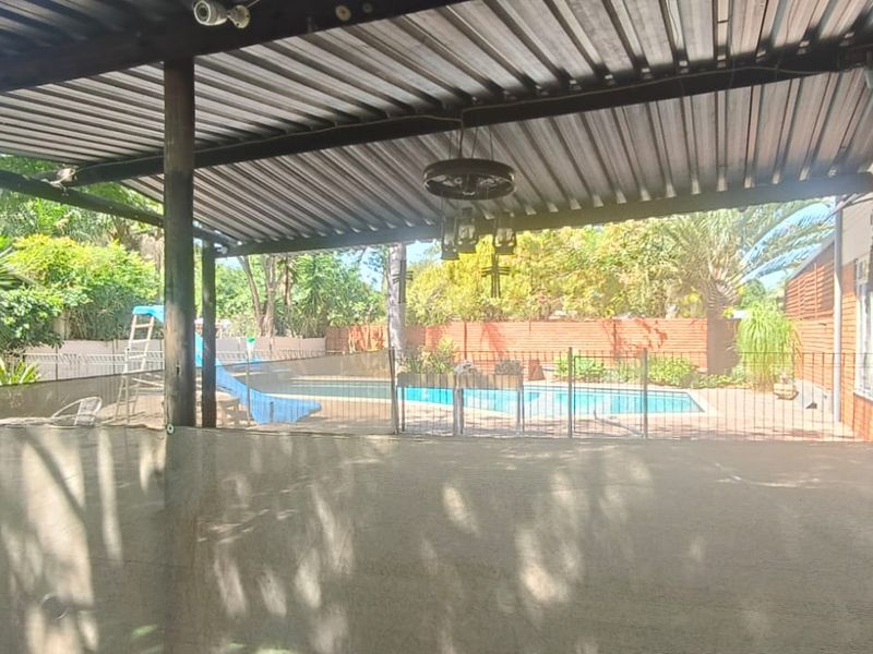 Covered outdoor patio area featuring a corrugated metal roof, overlooking a fenced swimming pool and garden space.
