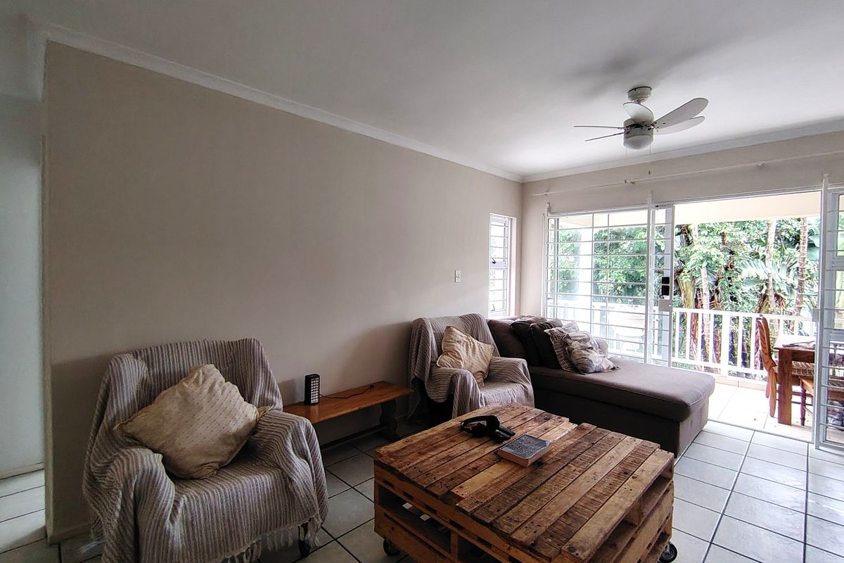 A bright living room featuring tiled flooring, a ceiling fan, and large sliding glass doors that open onto a private balcony.