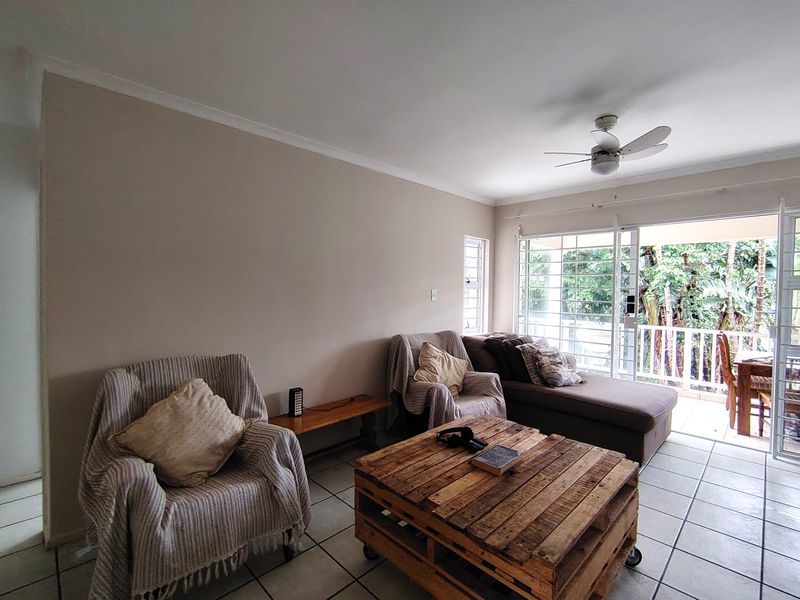 A bright living room featuring tiled flooring, a ceiling fan, and large sliding glass doors that open onto a private balcony.