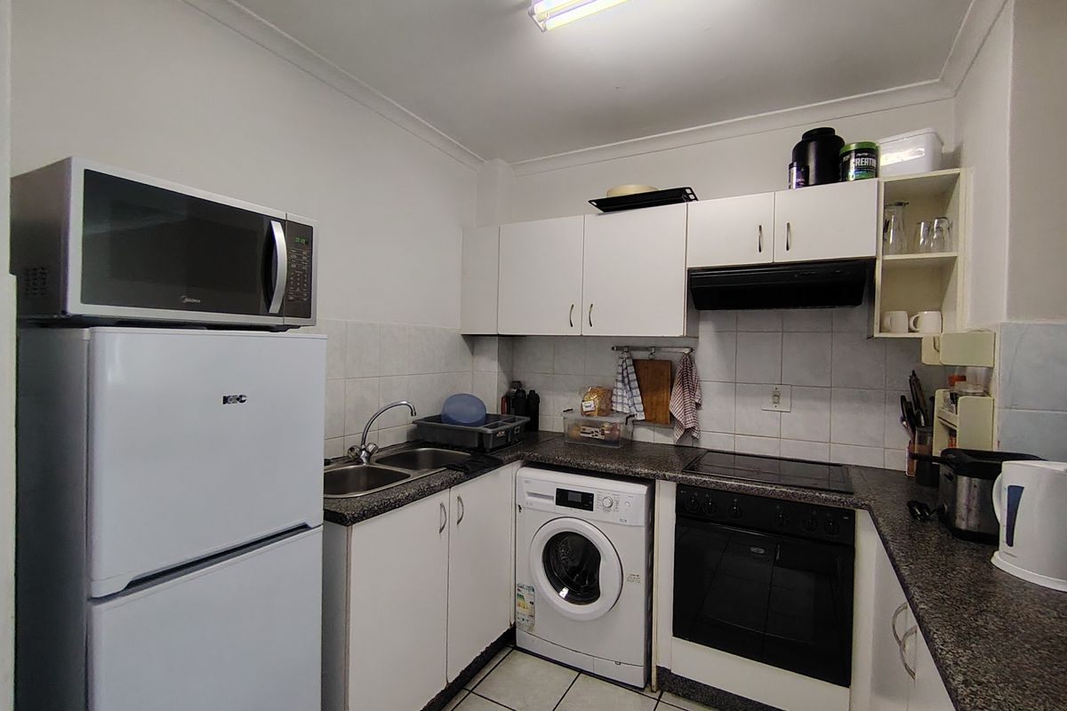 Compact kitchen featuring white cabinetry, laminate countertops, integrated oven and hob, and tiled flooring with a functional layout.