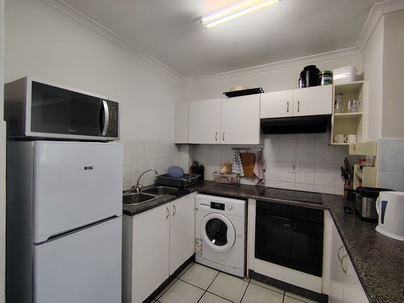 Compact kitchen featuring white cabinetry, laminate countertops, integrated oven and hob, and tiled flooring with a functional layout.