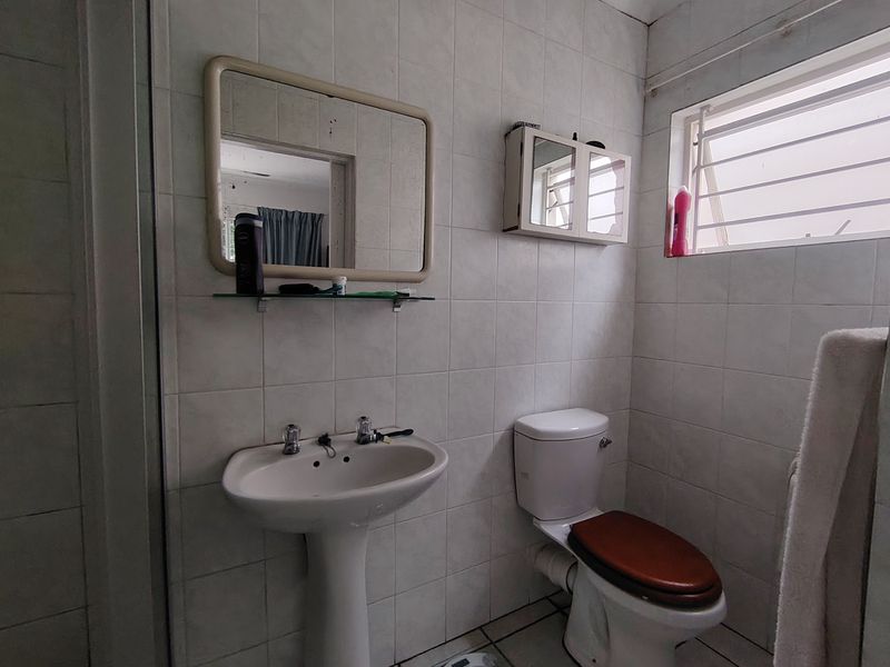 A functional bathroom featuring a pedestal basin, toilet, and wall-mounted medicine cabinet, finished with neutral wall and floor tiling.
