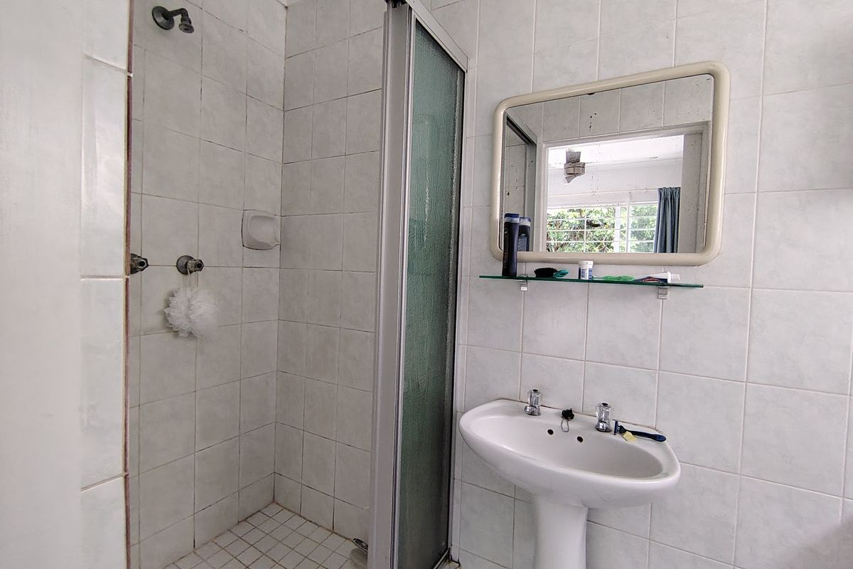 A functional bathroom featuring a pedestal basin, a tiled shower enclosure with a glass door, and wall-mounted mirror.