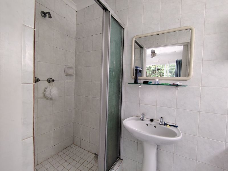 A functional bathroom featuring a pedestal basin, a tiled shower enclosure with a glass door, and wall-mounted mirror.