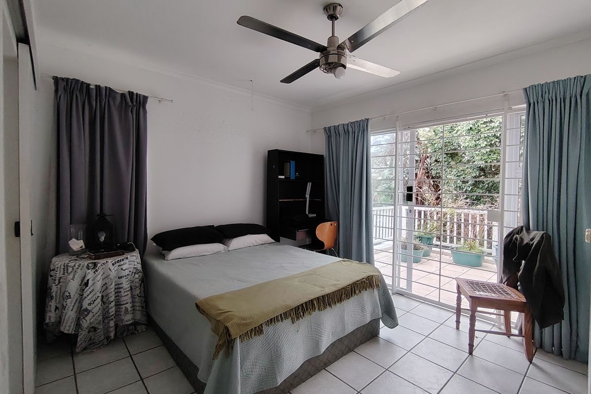 A bedroom featuring tiled flooring, a ceiling fan, and sliding glass doors that provide direct access to an outdoor balcony area.