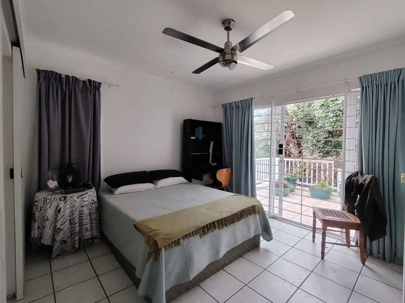 A bedroom featuring tiled flooring, a ceiling fan, and sliding glass doors that provide direct access to an outdoor balcony area.