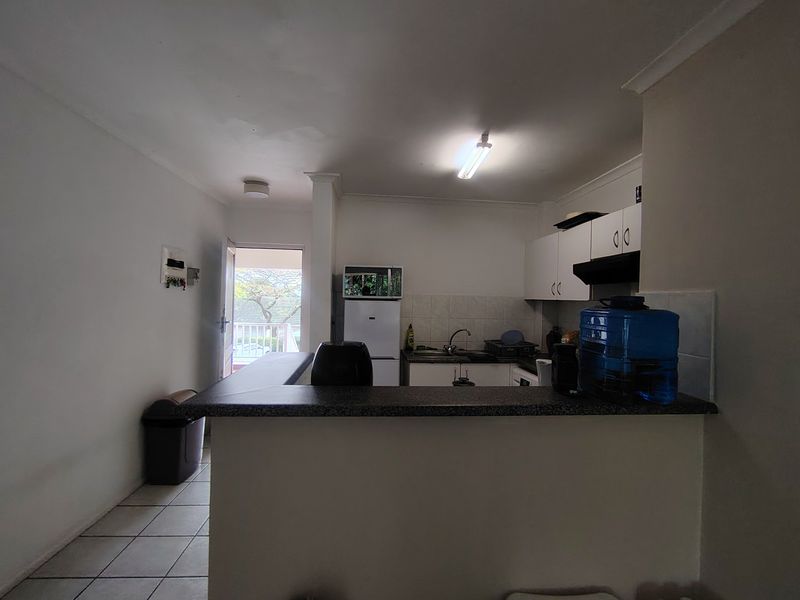 Open plan kitchen area featuring a breakfast bar, tiled flooring, and functional cabinetry, with direct access to an outdoor balcony space.