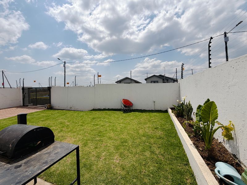 A private backyard featuring a well-maintained lawn, a raised garden bed, and secure perimeter walling with electric fencing.
