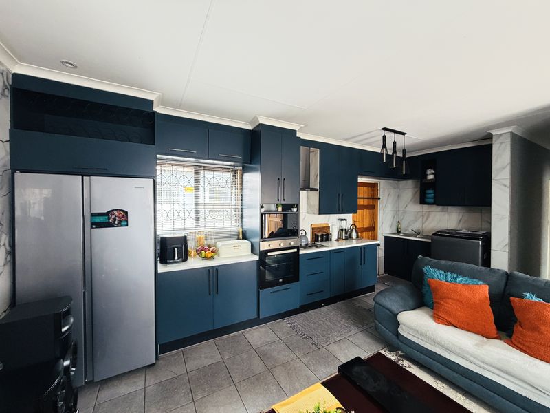 Modern open-plan kitchen featuring dark blue cabinetry, stone-look backsplash, integrated oven, and tiled flooring, seamlessly flowing into the living area.