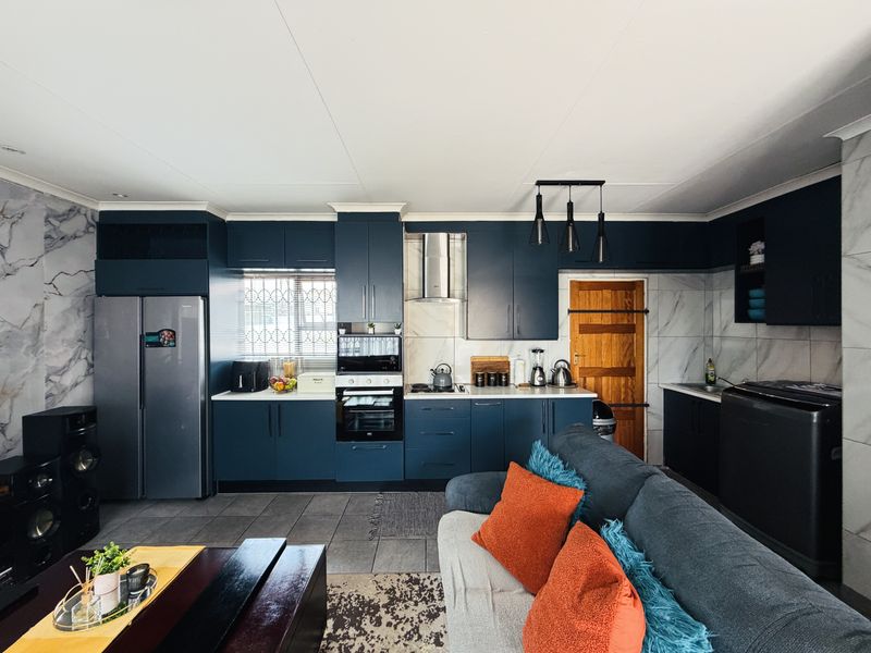 Modern open-plan kitchen featuring dark blue cabinetry, integrated appliances, marble-effect wall tiling, and tiled flooring, seamlessly connecting to the living area.