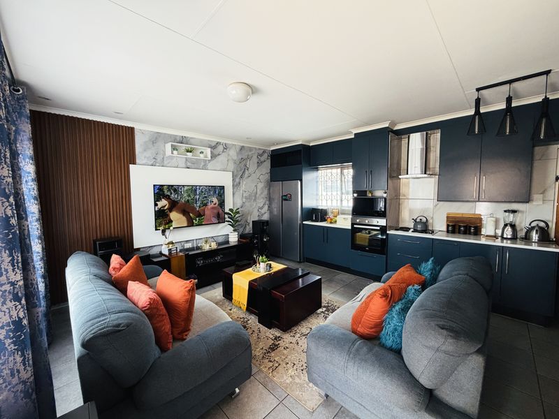 Modern open-plan living area featuring a contemporary kitchen with dark cabinetry, integrated appliances, and a stylish feature wall with built-in entertainment unit.