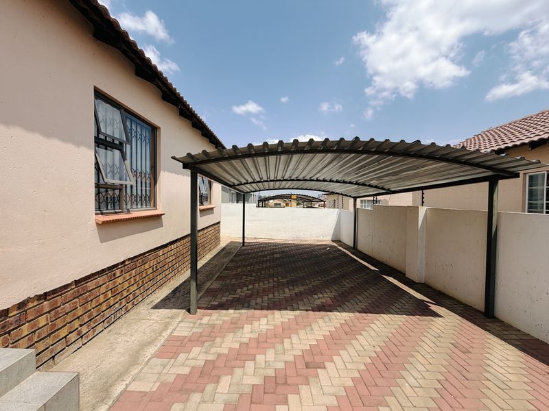 A covered carport area with paved flooring, situated alongside the main house structure with secure boundary walls.