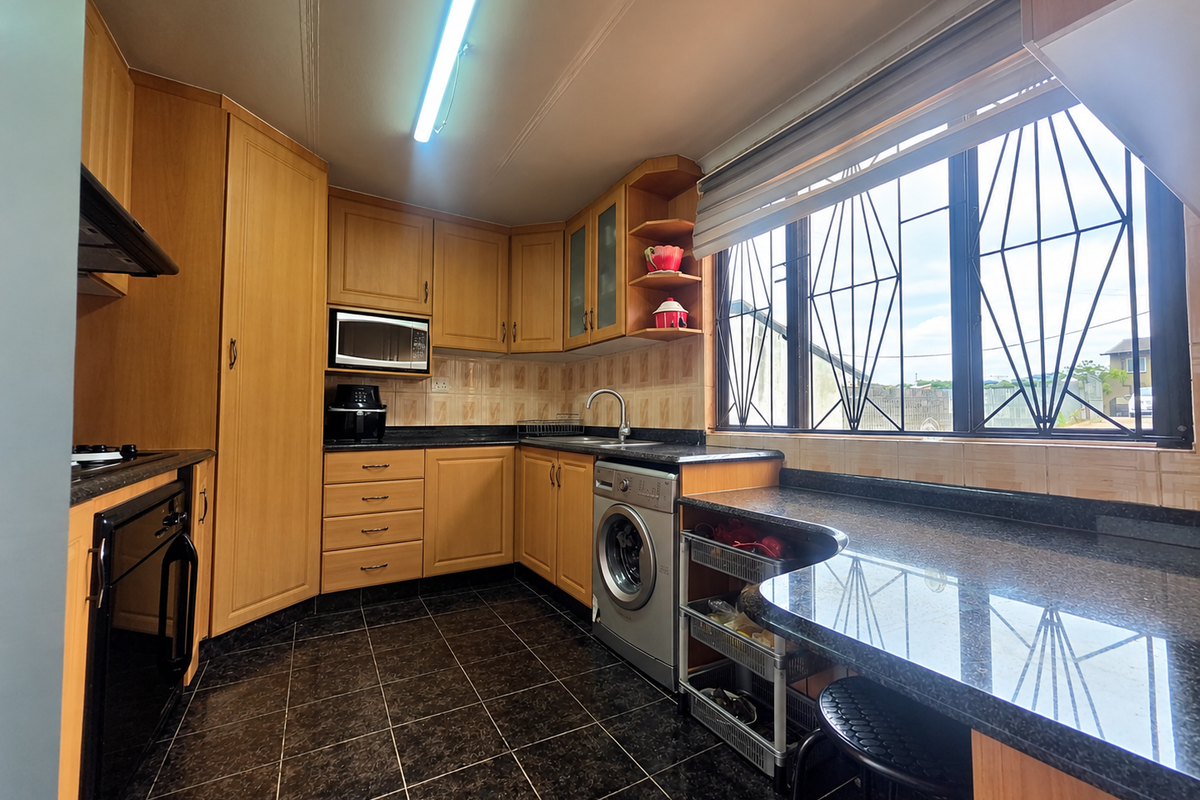 A functional kitchen featuring wood-finish cabinetry, granite countertops, integrated appliances, and large windows with security bars, providing ample workspace and natural light.