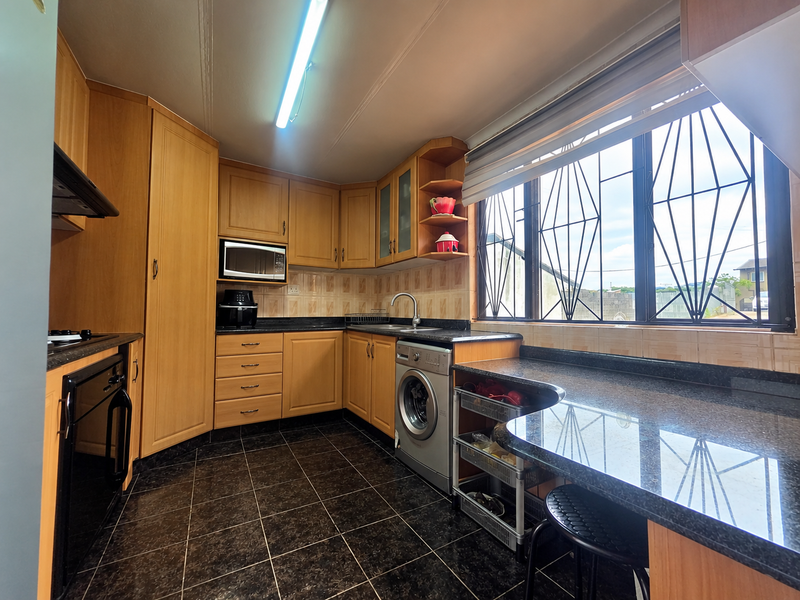 A functional kitchen featuring wood-finish cabinetry, granite countertops, integrated appliances, and large windows with security bars, providing ample workspace and natural light.