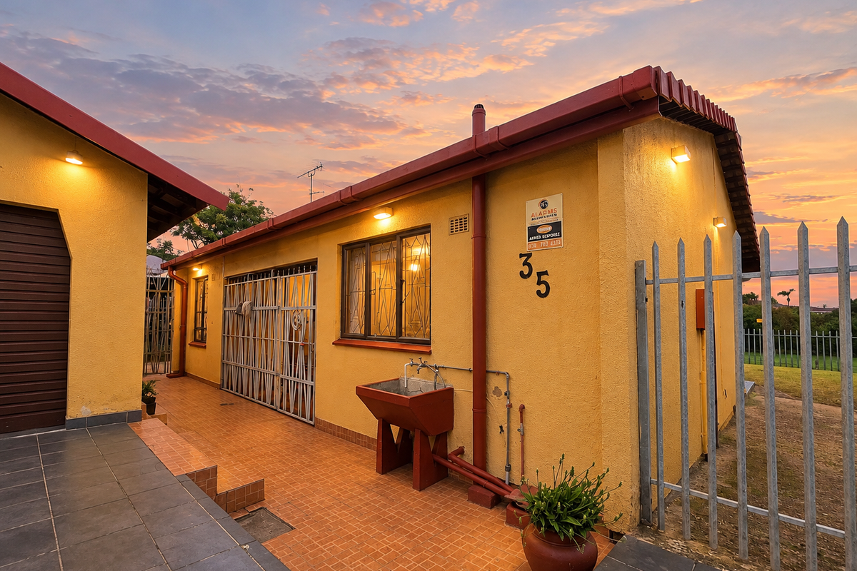 Rear exterior view of the property featuring a tiled patio area, security gates, and an external utility sink against a yellow rendered wall.