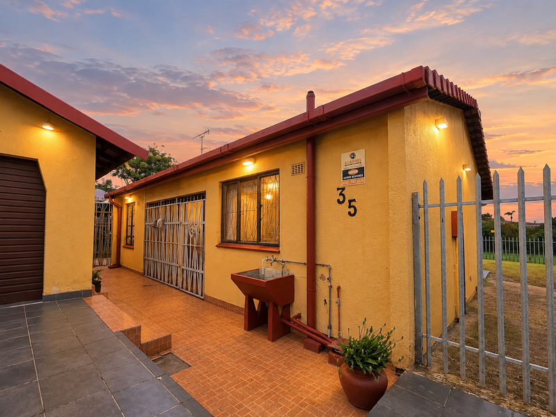 Rear exterior view of the property featuring a tiled patio area, security gates, and an external utility sink against a yellow rendered wall.