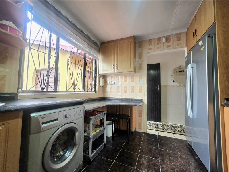 Functional kitchen featuring laminate cabinetry, granite-look countertops, tiled backsplash, and dedicated space for laundry appliances with security bars on the window.
