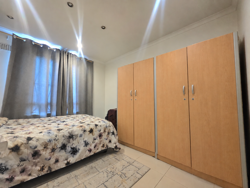 A well-lit bedroom featuring neutral tiled flooring, recessed downlighting, and extensive built-in wooden cabinetry for storage.