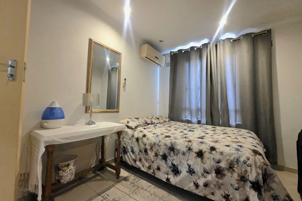 A functional bedroom featuring tiled flooring, recessed downlighting, and a wall-mounted split-system air conditioning unit.