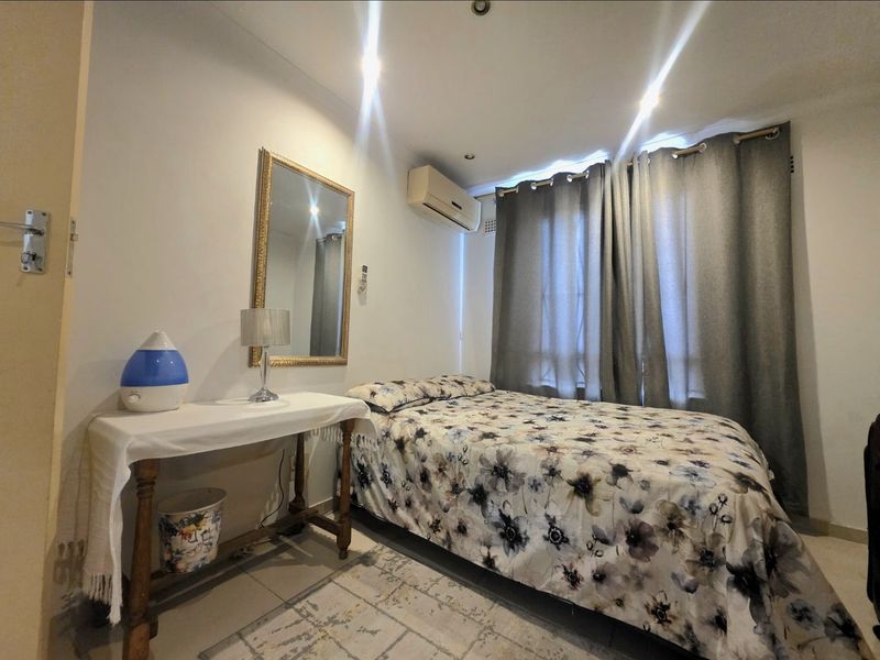A functional bedroom featuring tiled flooring, recessed downlighting, and a wall-mounted split-system air conditioning unit.