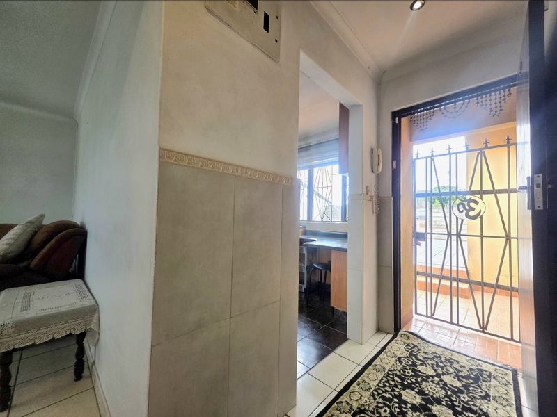 Entrance area featuring tiled flooring, coving, and a security gate, providing a view into the adjacent kitchen space.
