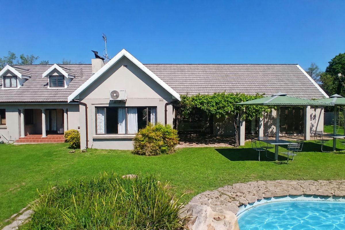Rear view of the house featuring a tiled roof, covered patio area, and a swimming pool set within a spacious garden.