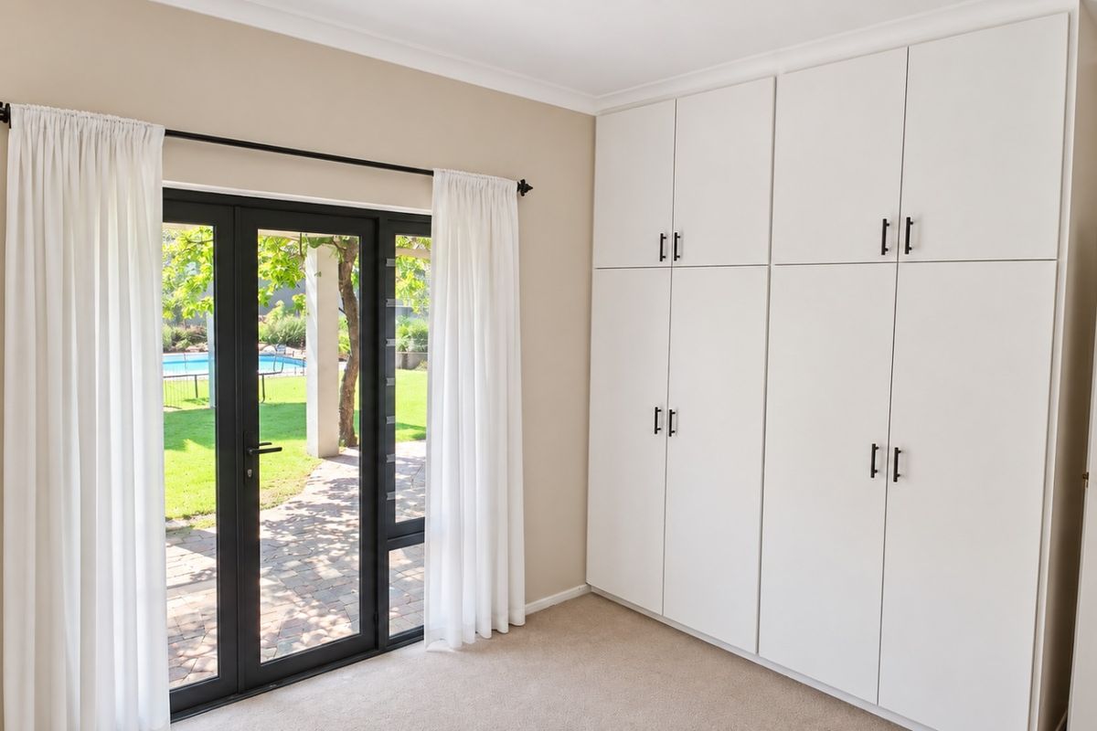 A bright bedroom featuring extensive built-in storage, neutral carpeting, and direct access to the garden through a modern glass door.