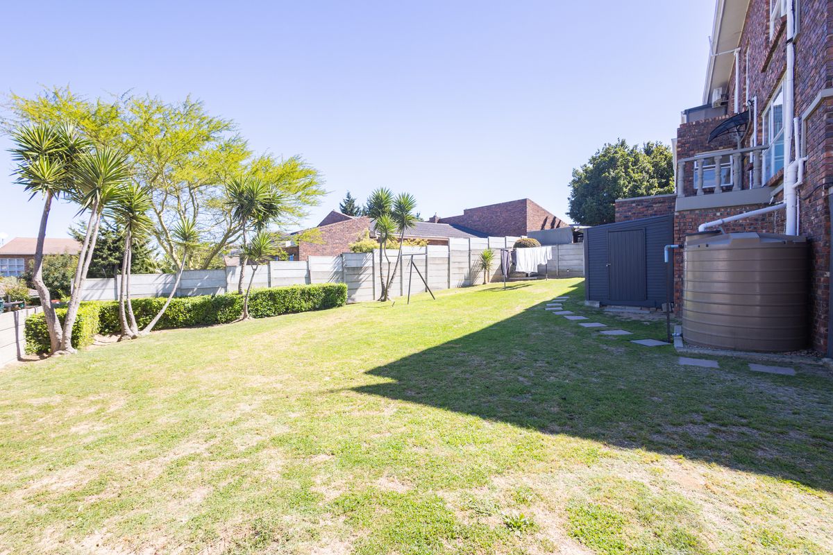 A spacious rear garden featuring a lawn, mature trees, a water storage tank, and a precast concrete boundary wall.
