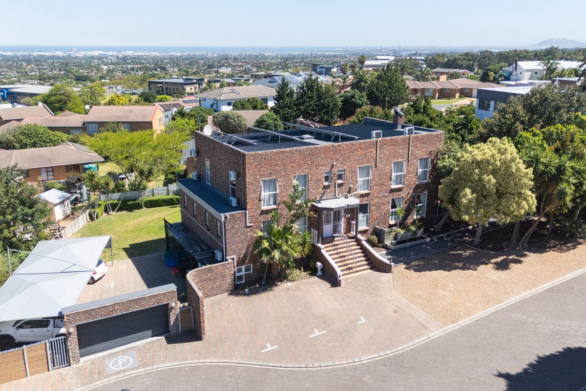 Aerial view of a multi-story brick residential building featuring a paved driveway, carport, garage, and rooftop solar panels in a suburban setting.