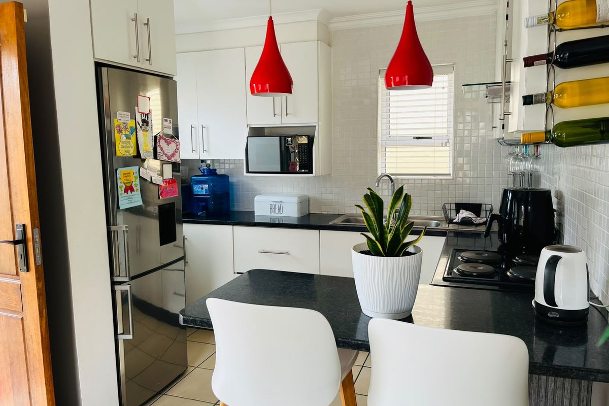 A functional kitchen featuring white cabinetry, black granite countertops, a built-in hob, and a tiled backsplash, offering a clean and practical cooking space.