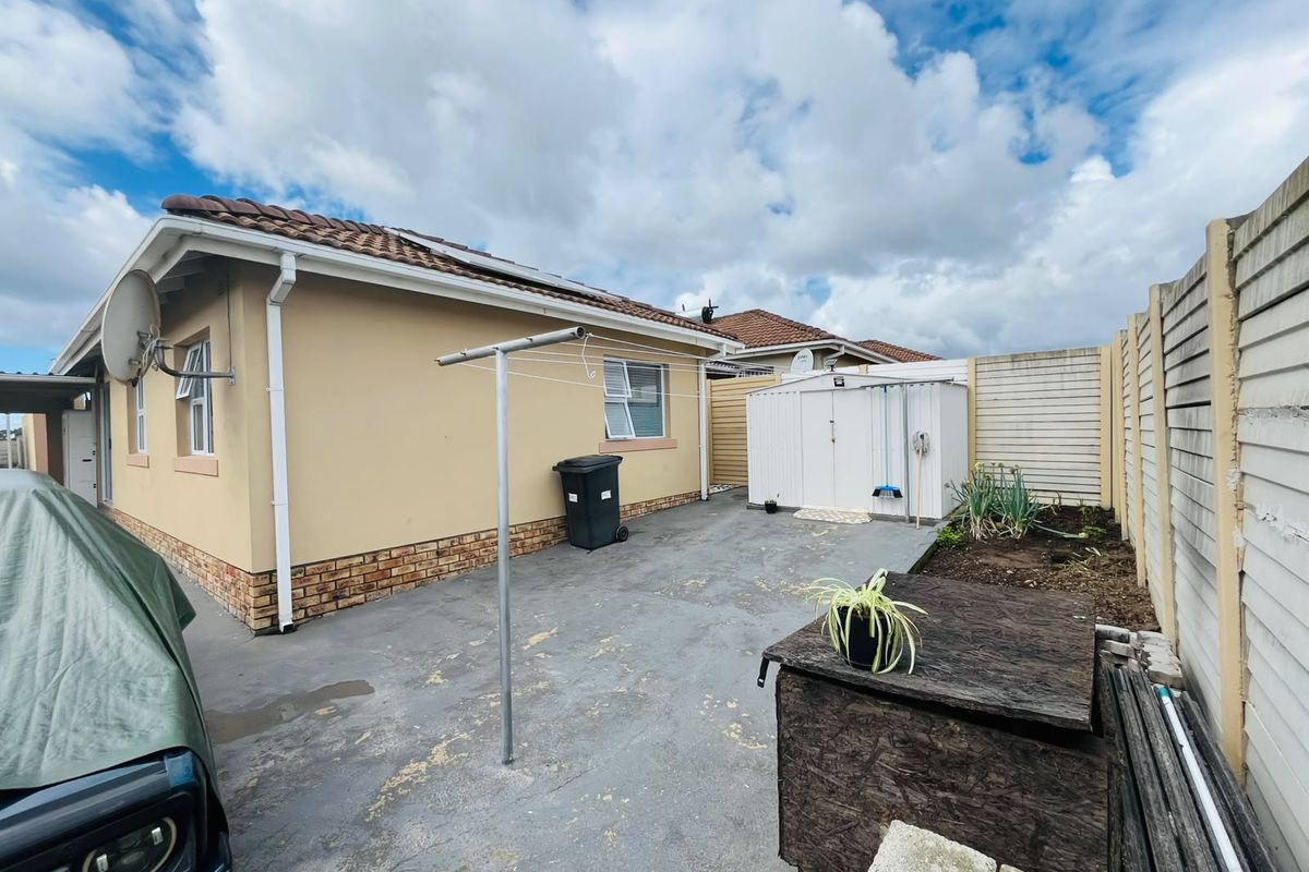 Rear exterior view of the townhouse featuring a concrete paved yard, a metal storage shed, and a precast concrete boundary wall.