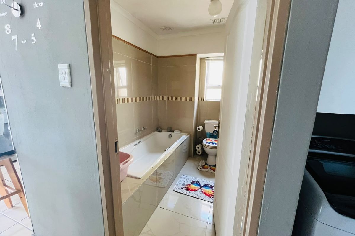 A functional bathroom featuring a built-in bathtub, ceramic tiling, and a toilet, viewed from the doorway.