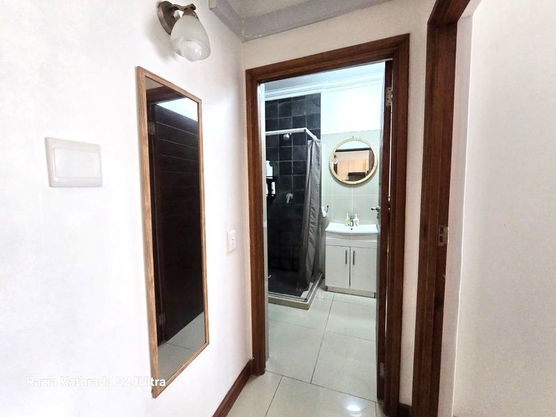 A view from a hallway looking into a bathroom featuring a vanity cabinet, shower enclosure, and tiled flooring.