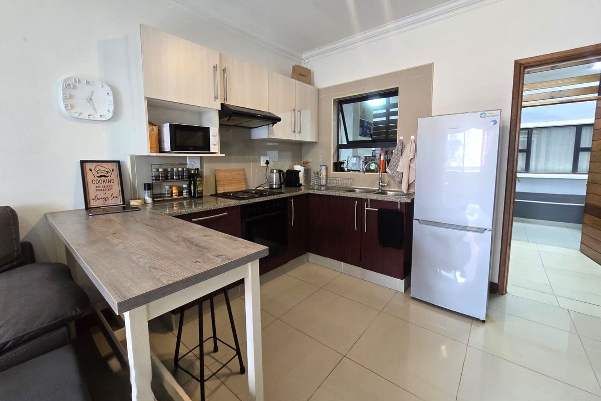 A functional kitchen featuring two-tone cabinetry, granite countertops, built-in oven with extractor fan, and tiled flooring.