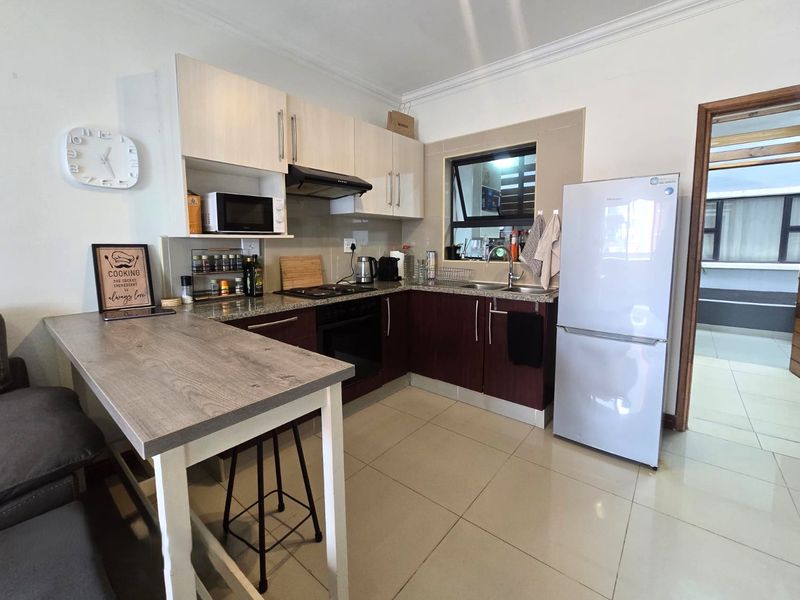 A functional kitchen featuring two-tone cabinetry, granite countertops, built-in oven with extractor fan, and tiled flooring.