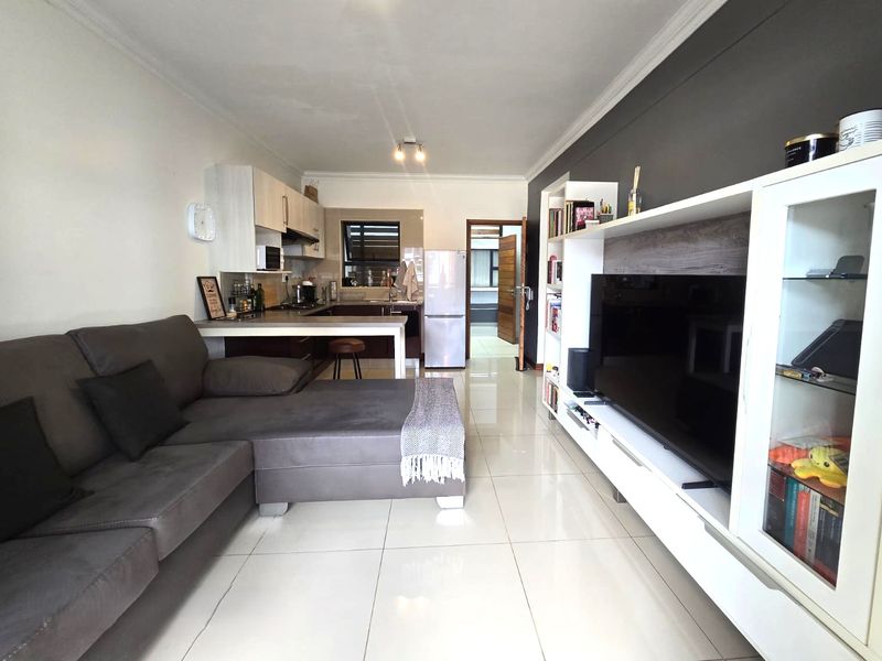 Open-plan living area featuring a modern kitchen with built-in cabinetry and sleek tiled flooring, seamlessly connecting to the lounge space.