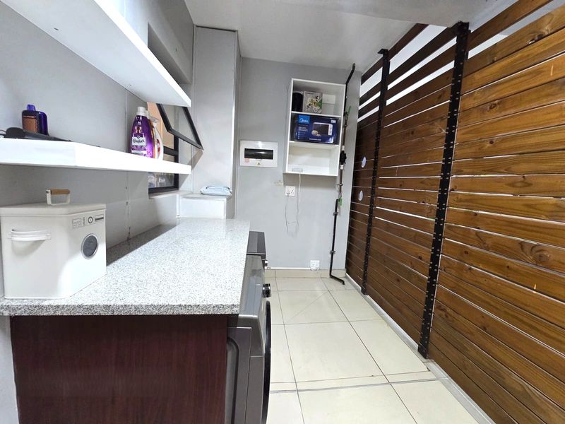 A functional laundry area featuring tiled flooring, granite countertops, built-in shelving, and a decorative timber slat wall finish.