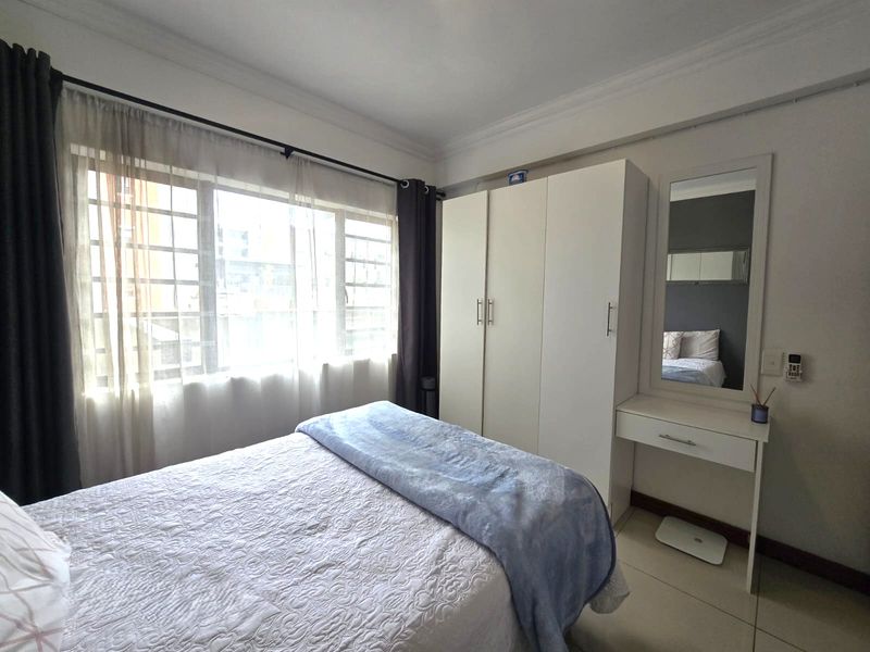 A well-maintained bedroom featuring tiled flooring, a built-in wardrobe, and large windows with security bars, providing ample natural light.