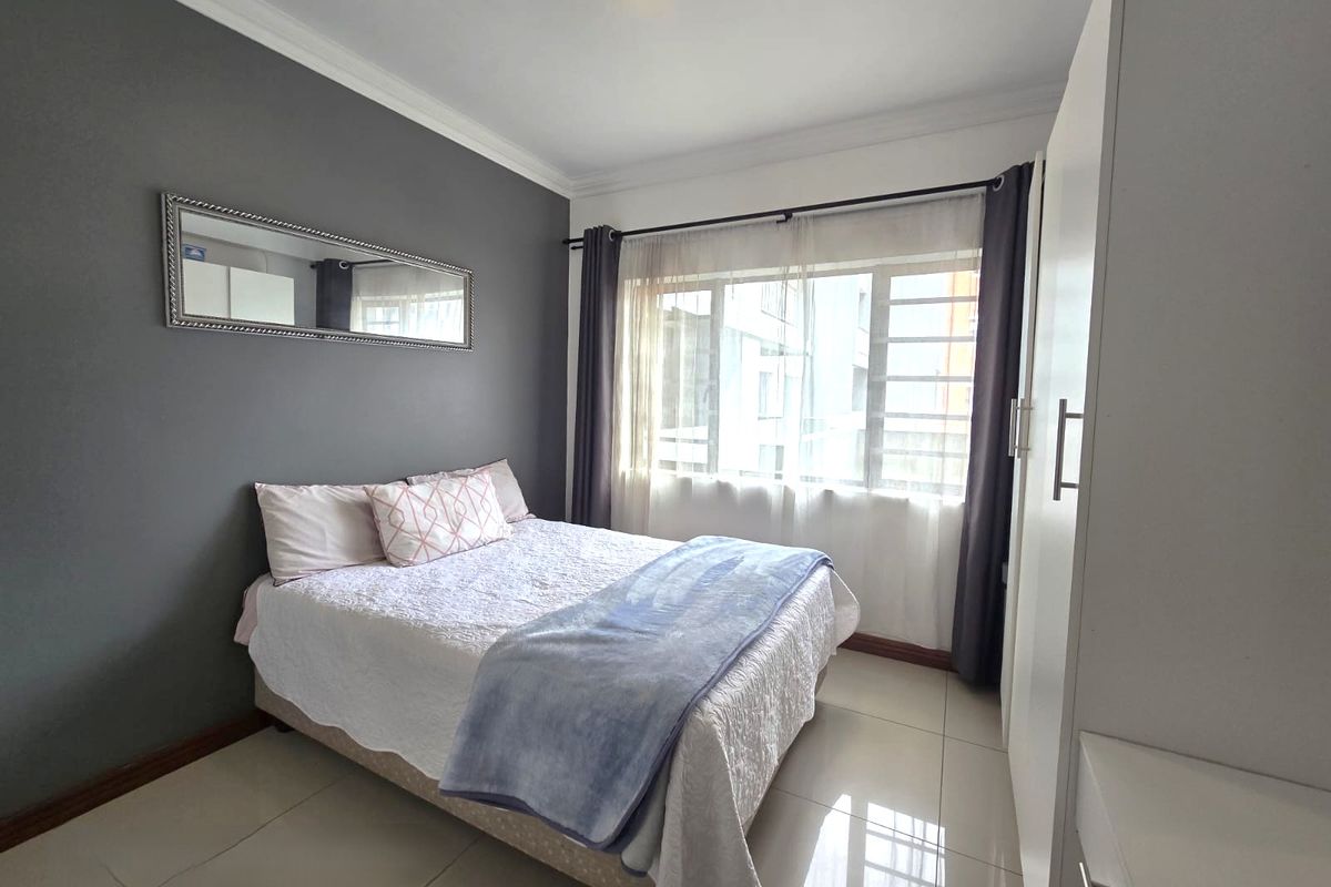 A well-maintained bedroom featuring tiled flooring, a built-in wardrobe, and a large window allowing for natural light.