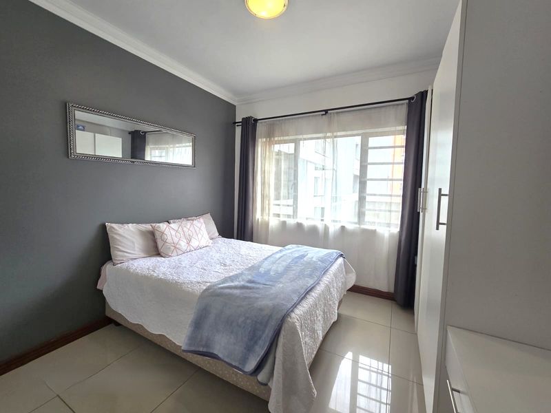 A well-maintained bedroom featuring tiled flooring, a built-in wardrobe, and a large window allowing for natural light.