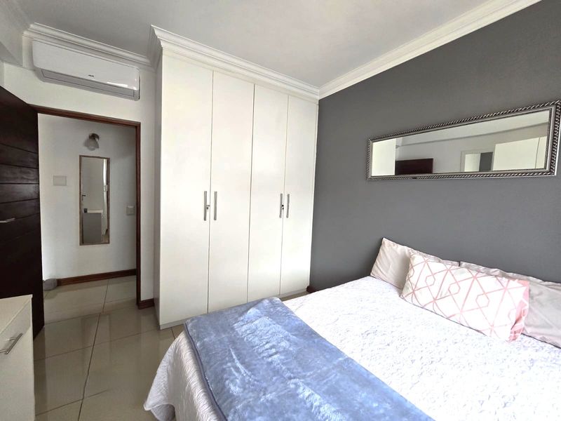 A well-maintained bedroom featuring built-in cupboards, tiled flooring, crown molding, and a wall-mounted air conditioning unit.