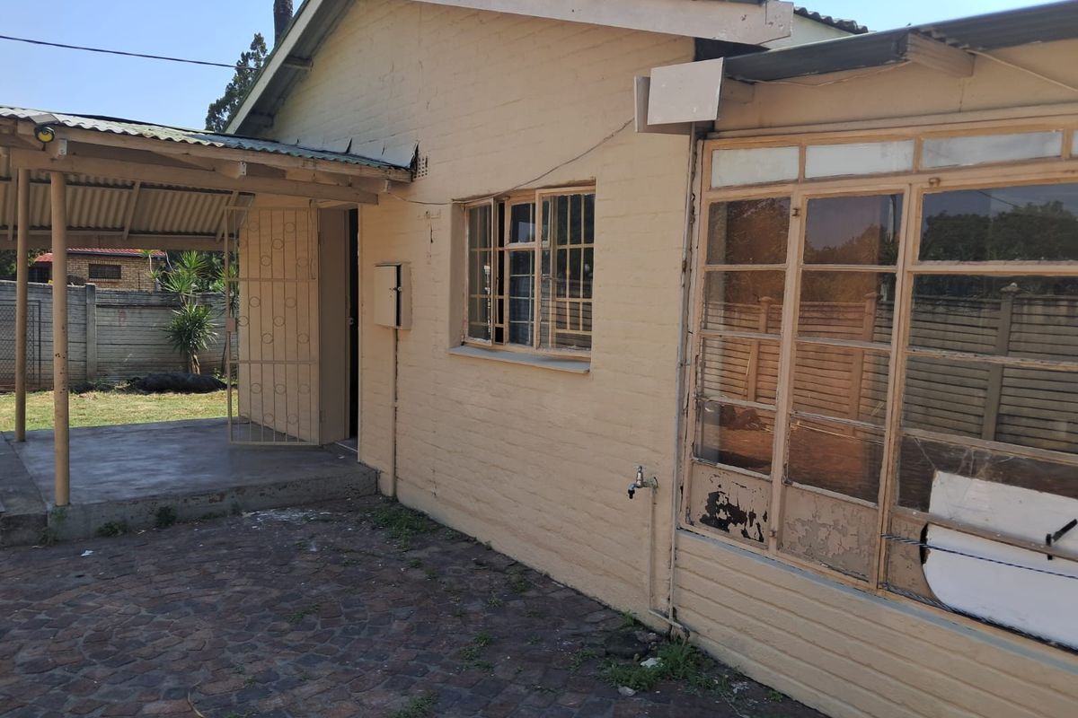 Rear exterior view showing a covered patio area, paved courtyard, and brick facade with security gate and window access.