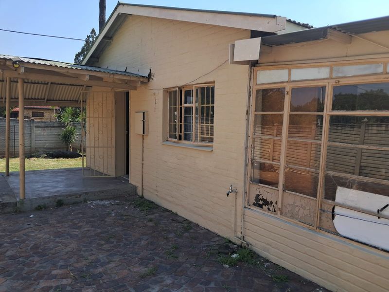 Rear exterior view showing a covered patio area, paved courtyard, and brick facade with security gate and window access.