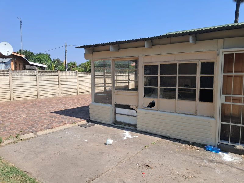 Rear exterior view showing a concrete patio and a dated, weathered timber-framed enclosure requiring significant maintenance and repair.