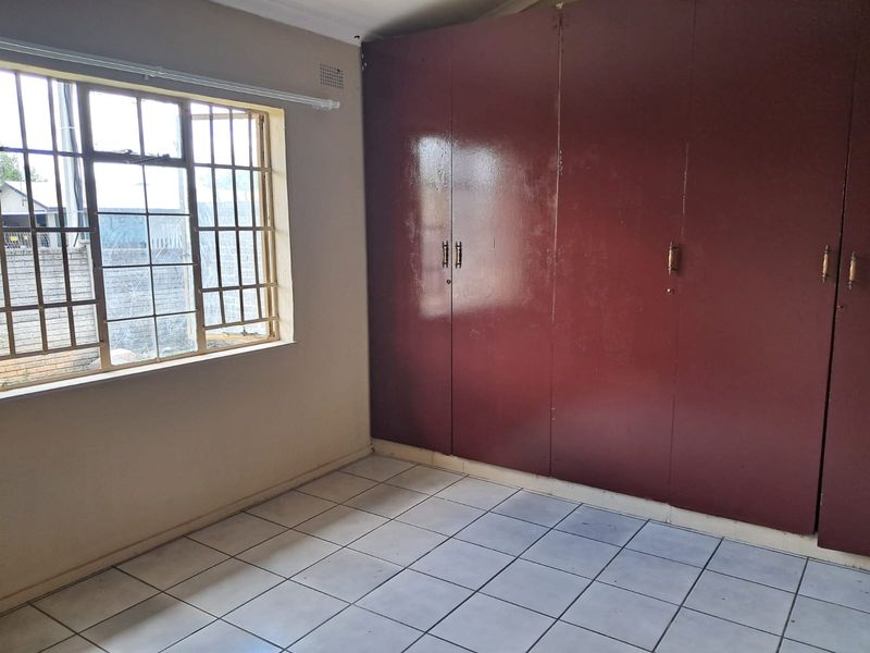 An empty bedroom featuring tiled flooring and extensive built-in cupboards, providing ample storage space. The room includes security bars on the window.