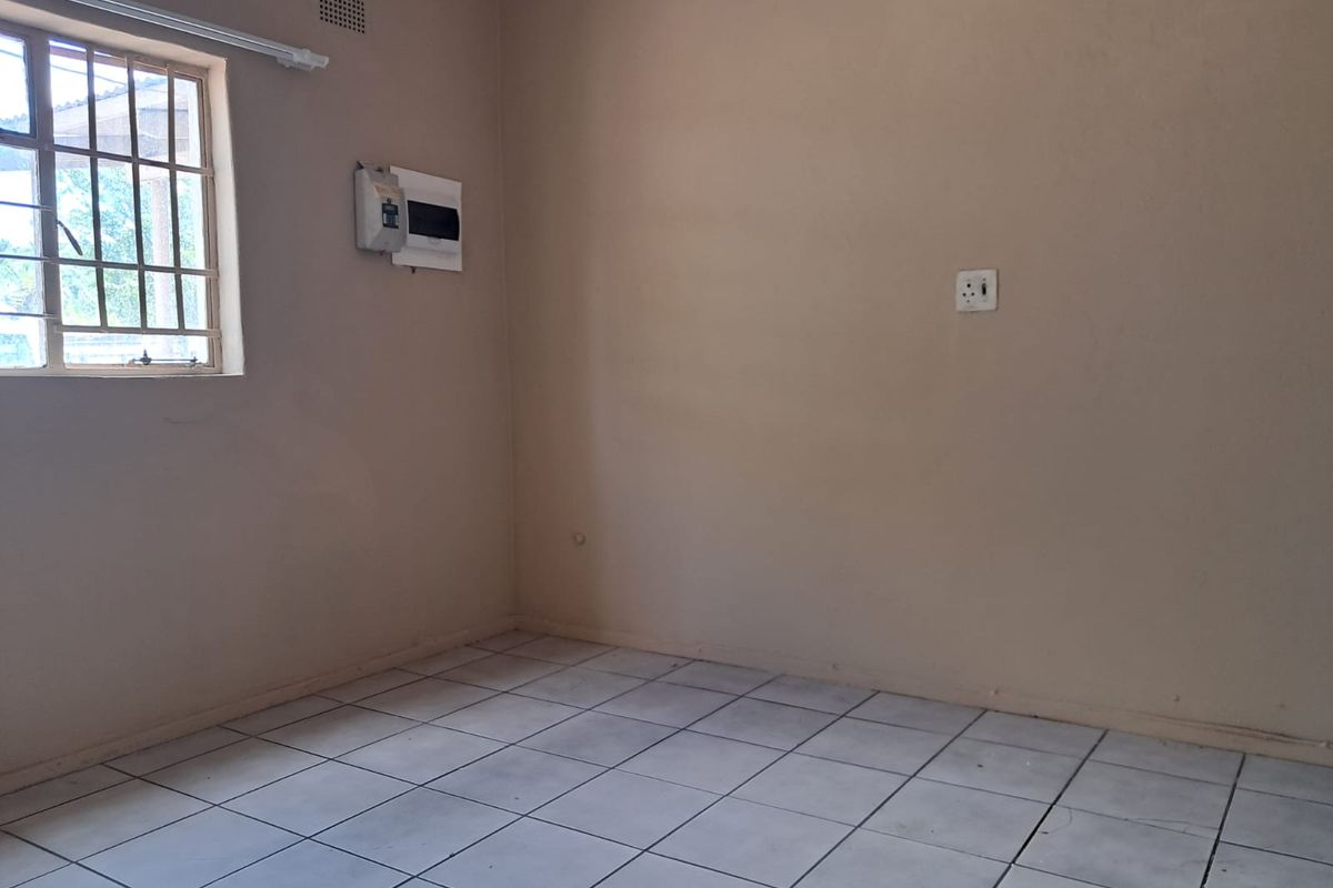 An empty bedroom featuring tiled flooring, a window with security bars, and an exposed electrical distribution board.