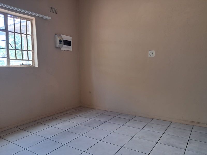 An empty bedroom featuring tiled flooring, a window with security bars, and an exposed electrical distribution board.