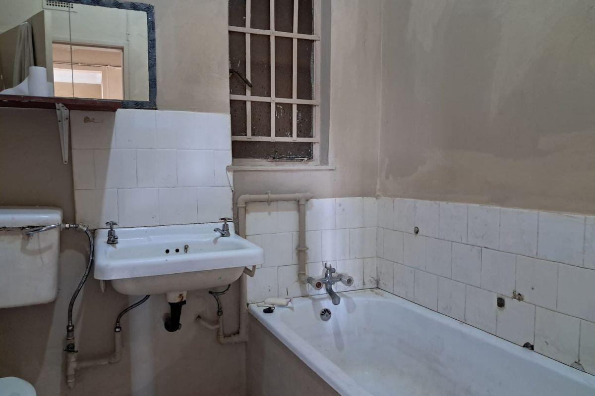 A dated bathroom featuring a wall-mounted basin, bathtub, and toilet cistern, requiring significant renovation and modernization of finishes and fixtures.