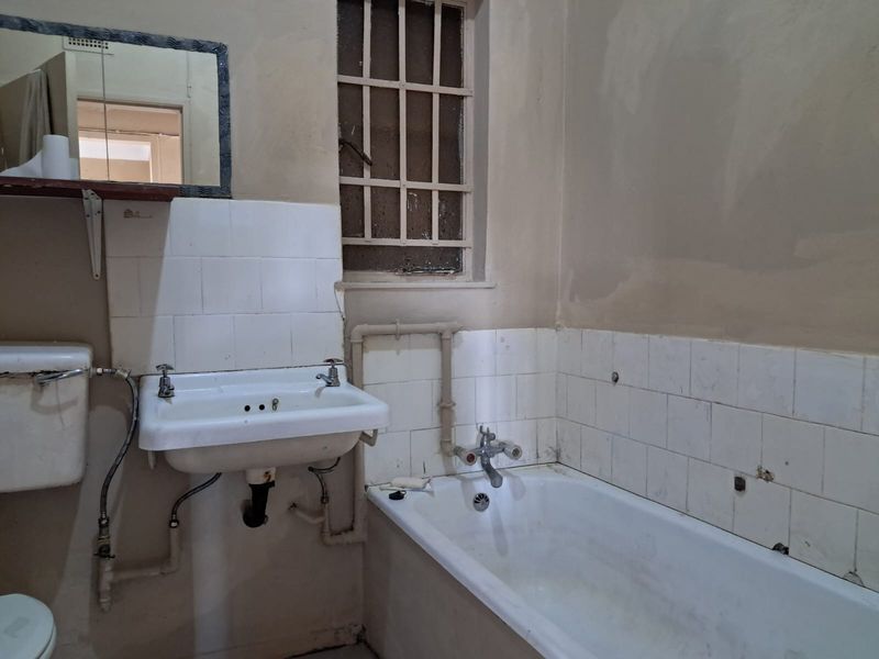 A dated bathroom featuring a wall-mounted basin, bathtub, and toilet cistern, requiring significant renovation and modernization of finishes and fixtures.