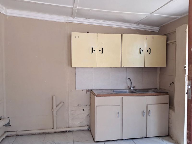 A basic kitchen area featuring built-in cabinetry, a stainless steel sink, and tiled splashback, requiring cosmetic updates and finish improvements.